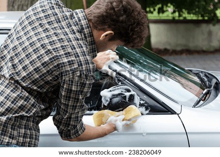 Young man accurately cleaning wing mirror in his car