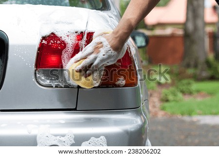 Man\'s hand polishing rear lights of silver car by sponge