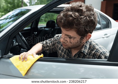 Young handsome owner of silver car waxing car door