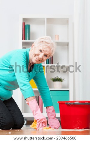 Active elderly lady cleaning the floor on her knees