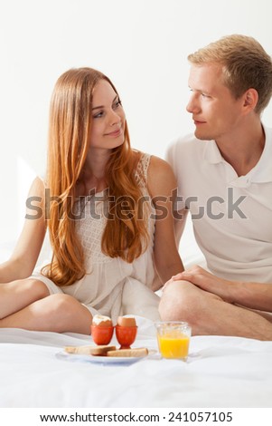 Young smiley couple in bed having breakfast
