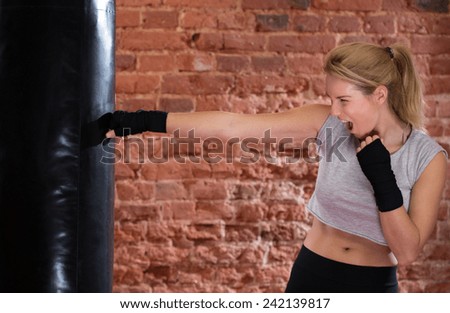 Young strong screaming woman punching the training bag