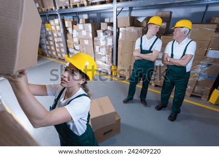 Hardworking woman and lazy co-workers in warehouse