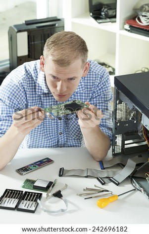 Young intelligent man fixing up damaged computer