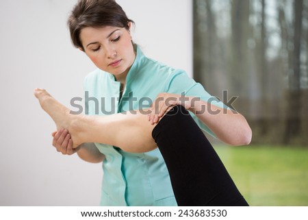 Young pretty female physiotherapist flexing patient\'s knee
