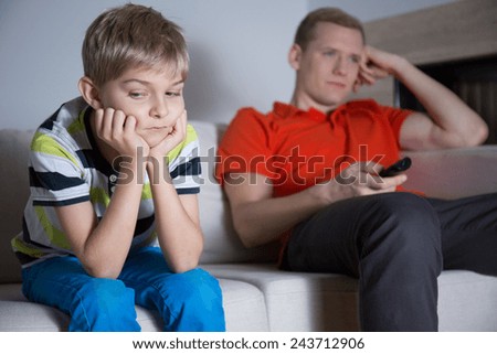 Bored child sitting on the sofa and his father watching tv