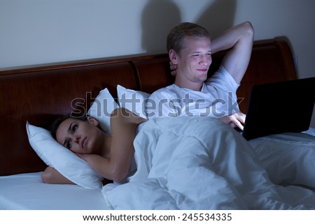 Sleepless wife and her husband with laptop in bed