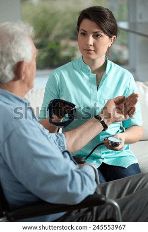 Young pretty nurse checking the older man\'s blood pressure