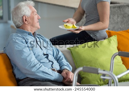 Young female caregiver giving the fruit to older man