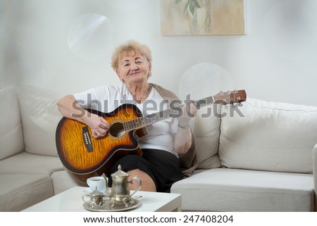 Senior woman being alone at home and playing the guitar