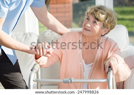 Young male therapist helping older woman to stand up