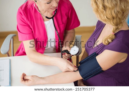 Experienced doctor checking young pregnant woman blood pressure
