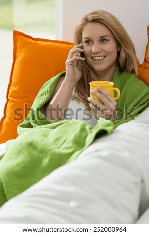 Young woman drinking tea in bed and talking on the phone