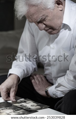 Old man in mourning watching pictures of his wife