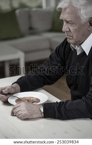 Elderly widower eating meal in loneliness in home