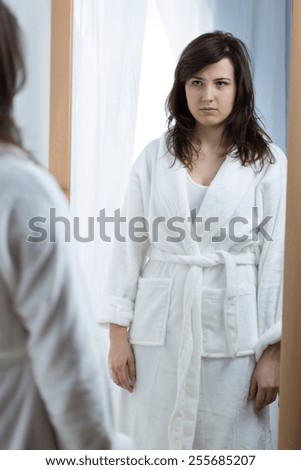 Young sad woman opposite the mirror without self confidence