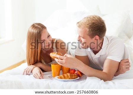Man feeding woman with croissant in bed