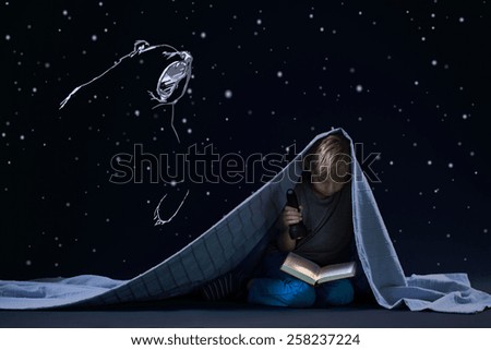 Little cute boy under quilt and his night\'s reading with torch
