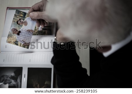Lonely windowed man watching photo album and recollecting