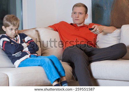 Young handsome father watching television and his angry son
