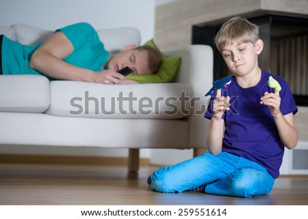 Sleeping father and little sad boy playing alone