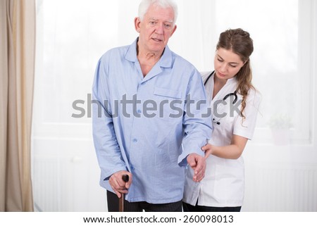 Patient using walking stick assisted by doctor