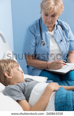 Female elderly doctor looking at sick sleeping boy