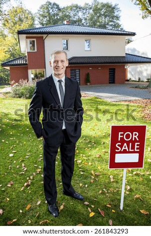 Estate broker is standing outside the house and smiling