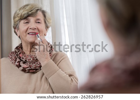 Portrait of senior lady applying red lipstick