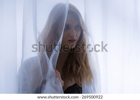 Close-up of blonde sensual woman behind the curtain