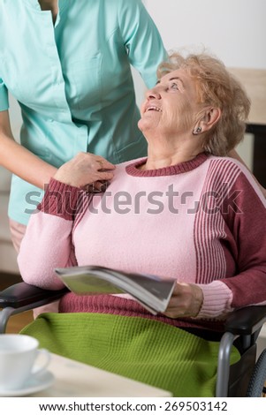 Old lady reading a magazine and smiling to a nurse