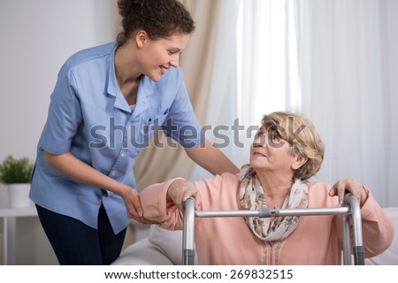 Senior woman using walking frame and supporting nurse