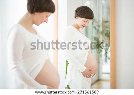Happy pregnant woman watching her naked belly