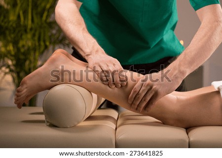 Close-up of masseur\'s hands kneading female calf