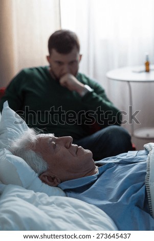 Ill father lying in hospital bed and his worried son