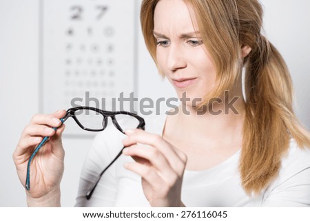 Young pretty confused woman looking at new glasses