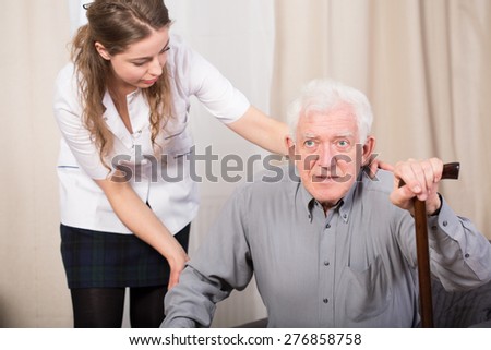 Careful female caregiver helping older man to stand up