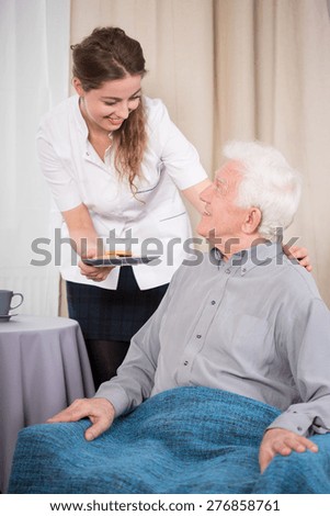 Young caring nurse giving the dessert to older nice man