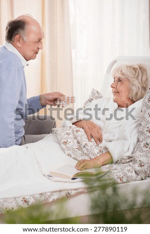 Ill senior woman in bed and assisting husband