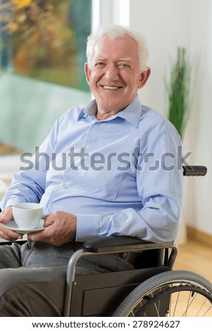Happy elder man on wheelchair drinking coffee