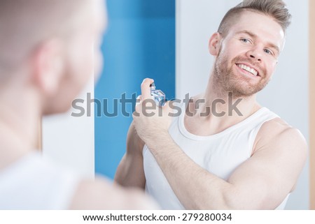 Reflection of smiling handsome guy applying perfume