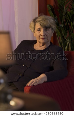 Elderly sad lady sitting in solitude in dark room