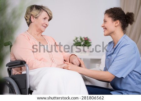Young pretty thoughtful nurse and older lady on wheelchair