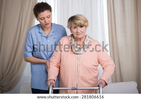 Aged disabled lady with walker and her helpful caregiver