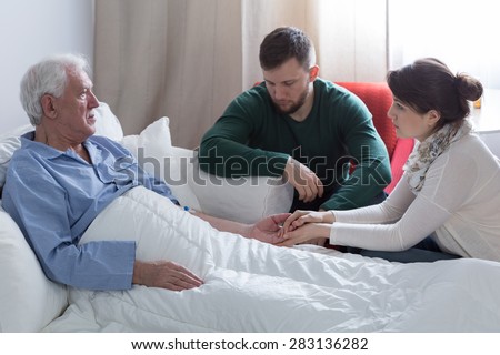 Supportive adult kids and terminally ill dad in bed