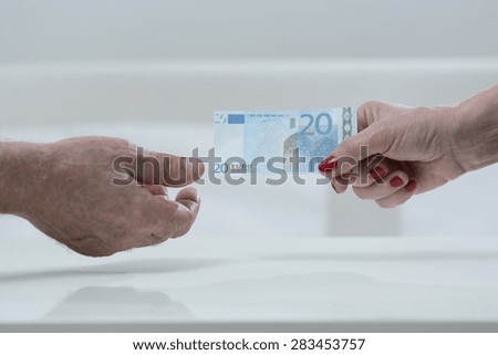Elder woman handing an euro banknote to elder man