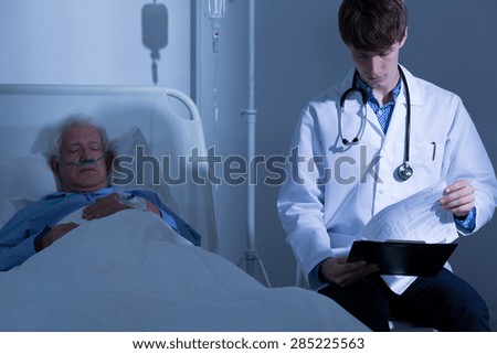 Young physician looking at his terminally ill patient\'s medical history