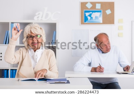 Senior student sitting at the desk and raising hand