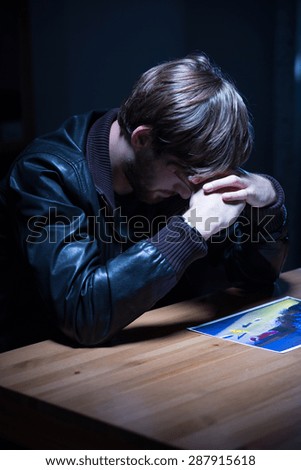 Sad man looking at picture in interrogation room
