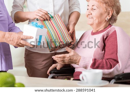 Two women giving the colorful presents to older lady on wheelchair